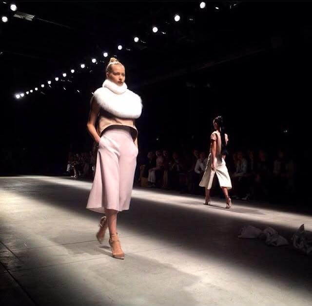 A model in a spotlight on the runway wearing a shearling collar and blush culottes, designed by Federica Cavenati